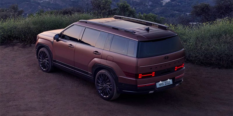 Rear side view of a bronze Hyundai parked on a dirt road